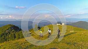 DRONE: Extreme mountain bikers pedalling their bicycles up a steep grassy hill.