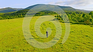 Drone flies above guy walks on grassland