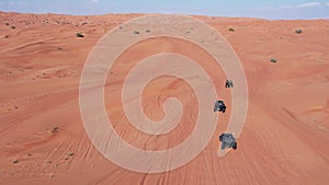 A drone flies over a caravan of buggies driving through the desert sand