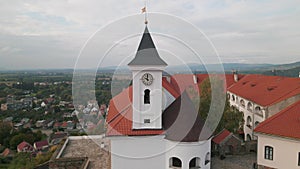 Drone flies over clock tower in medieval castle on mountain in small european city at cloudy autumn day