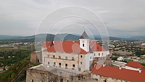 Drone flies over clock tower in medieval castle on mountain in small european city at cloudy autumn day