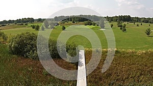 A drone flies over a green golf course with wooden bridge over a swamp