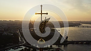 The drone flies to the golden angel on the cross of the Peter and Paul Fortress at sunrise, reflection of the orange sky