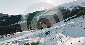 Drone flies towards ski lifts working in beautiful winter landscape mountains resort, sun rising on clear cold day.