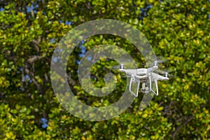 Drone in flight, green trees in the background, selective focus on the drone