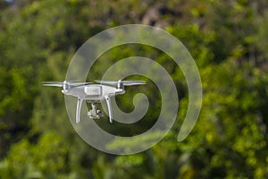 Drone in flight, green trees in the background, selective focus on the drone