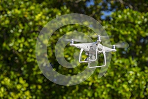 Drone in flight, green trees in the background, selective focus on the drone