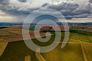 Drone flight at high altitude over a large field with many wind turbines spinning. The wind turbines cast a long shadow