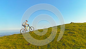 DRONE: Flying along an athletic man pedalling an e-bike up a steep grassy hill.