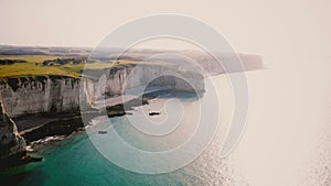 Drone flying along beautiful azure sea coastline on sunset and epic white chalk cliffs at sunny Etretat, Normandy.