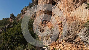 drone flying along limestone cliff with rock climber on it. man climbs challenging route on vertical crag