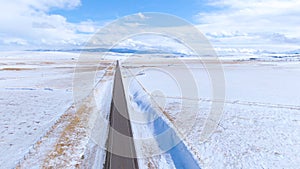 DRONE: Flying along a long straight road leading through the wintry Montana