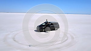 Drone flying close around excited couple at silver minivan car in the middle of amazing Bonneville salt desert road trip