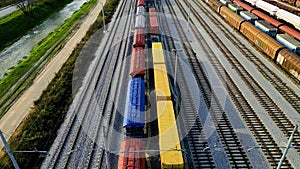 Drone flying directly above cargo trains with colorful wagons standing still at the station