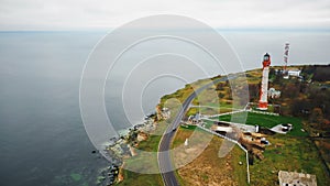 Drone flying high above car moving along road near beautiful old lighthouse bay and eroded sea coastline on overcast day