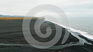 Drone flying over the coast of Iceland covered in black sand beaches on a cloudy day