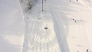 Drone flying over moving ski elevator on snowy slope in mountain resort. Top aerial view ski lift transporting skiers and snowboar