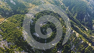 Drone flying over the series of serpentines road with moving cars, surrounded by green trees