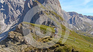 DRONE: Flying towards the cheerful female hiker taking photos of the mountains.