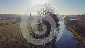 Drone flying up next to a river or canal and farm fields in Belgie around sunrise or sunset