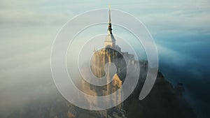 Drone flying very close near ethereal Mont Saint Michel island castle covered by atmospheric sunrise mist in Normandy.