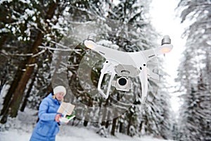 Drone flying at winter snowy forest piloted by young woman