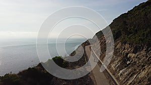 Drone following a motorbiker driving along on a curvy coastal empty road.