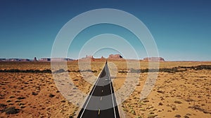 Drone follows silver car driving along famous sunny American desert highway road in Monuments Valley in Arizona and Utah