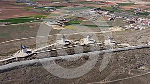 Drone footage approaching of three traditional windmills in a row in Consuegra in Toledo, Spain, with agricultural fields in the