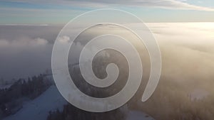 Drone footage of a flight over the hill of Vuokatinvaara, Kainuu, Finland., hiding in the dense fog at sunrise. View of snowy Finn