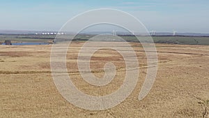 Drone footage over an empty field with a wind farm in the background