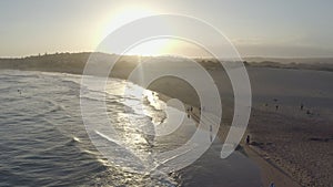 Drone, landscape and people at beach for sunset, waves and relax on sand at ocean. Water, nature and aerial view of sea