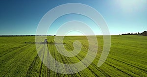 Drone moves to and flies over trailed sprayer under blue sky