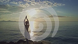 Drone moves to girl doing yoga against sunrise boundless sea