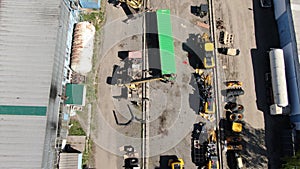 Drone moving along construction site with heavy machinery and shipping containers. Aerial top view of workers loading