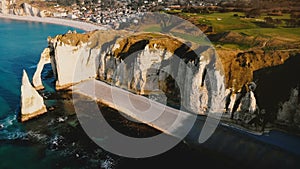 Drone panning right over beautiful sunset town of Etretat in Normandy revealing famous white chalk cliff coastline.