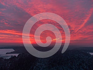 Drone panorama of amazing red sunrise behind clouds over bavarian forest and field area with snow in winter