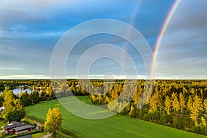 Drone photo, rainbow over summer pine tree forest,green wheat field, very clear skies and clean rainbow colors. Scandinavian