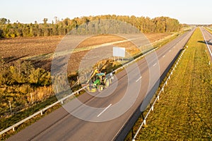 Drone photography of tractor mowing grass near a highway during autumn morning