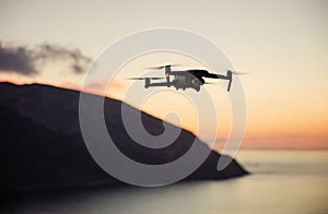 Drone quadcopter with digital camera flying over coast at sunset