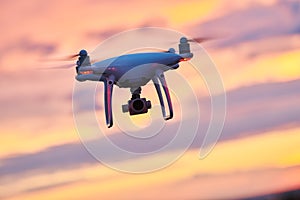 Drone quadcopter with digital camera flying at sunset