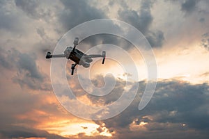 Drone quadcopter with digital camera flying at sunset