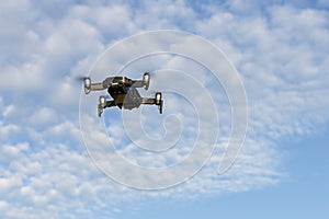 A drone, a quadrocopter with a camera for video shooting, flies against a blue sky with clouds