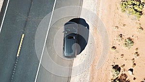 Drone quickly rising above car with sunroof open, standing on asphalt road in the middle of dry rocky American desert.