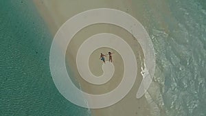 Drone rising above turquoise water and travel couple lying at the sandbar in Philippines