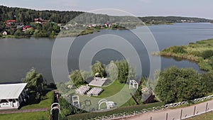 Drone shooting of the river with cottages on one bank and a site for a wedding ceremony on the other