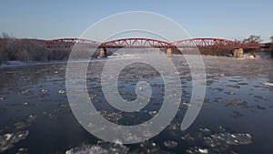 Drone Shot Flies Forward Over the Frozen River to the Red Steel Bridge, Aerial View 4k Video Footage