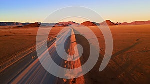 Drone shot from front of suv travelling through african desert. Aerial view of car with tourists moving through orange