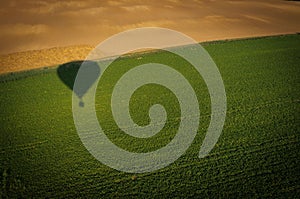 Drone shot of a hot air balloon shadow on a green field near Nitra, Slovakia in summer morning