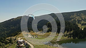 Drone shot of a man flying paramotor over an idyllic mountain lake landscape